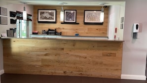 A reception desk with a wooden finish, framed artwork on the wall, and a hand sanitizer dispenser.