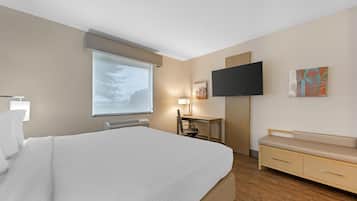 Ein Hotelzimmer mit einem großen Bett, einem Schreibtisch, einem Sessel, einem Fernseher und einer Sitzbank.