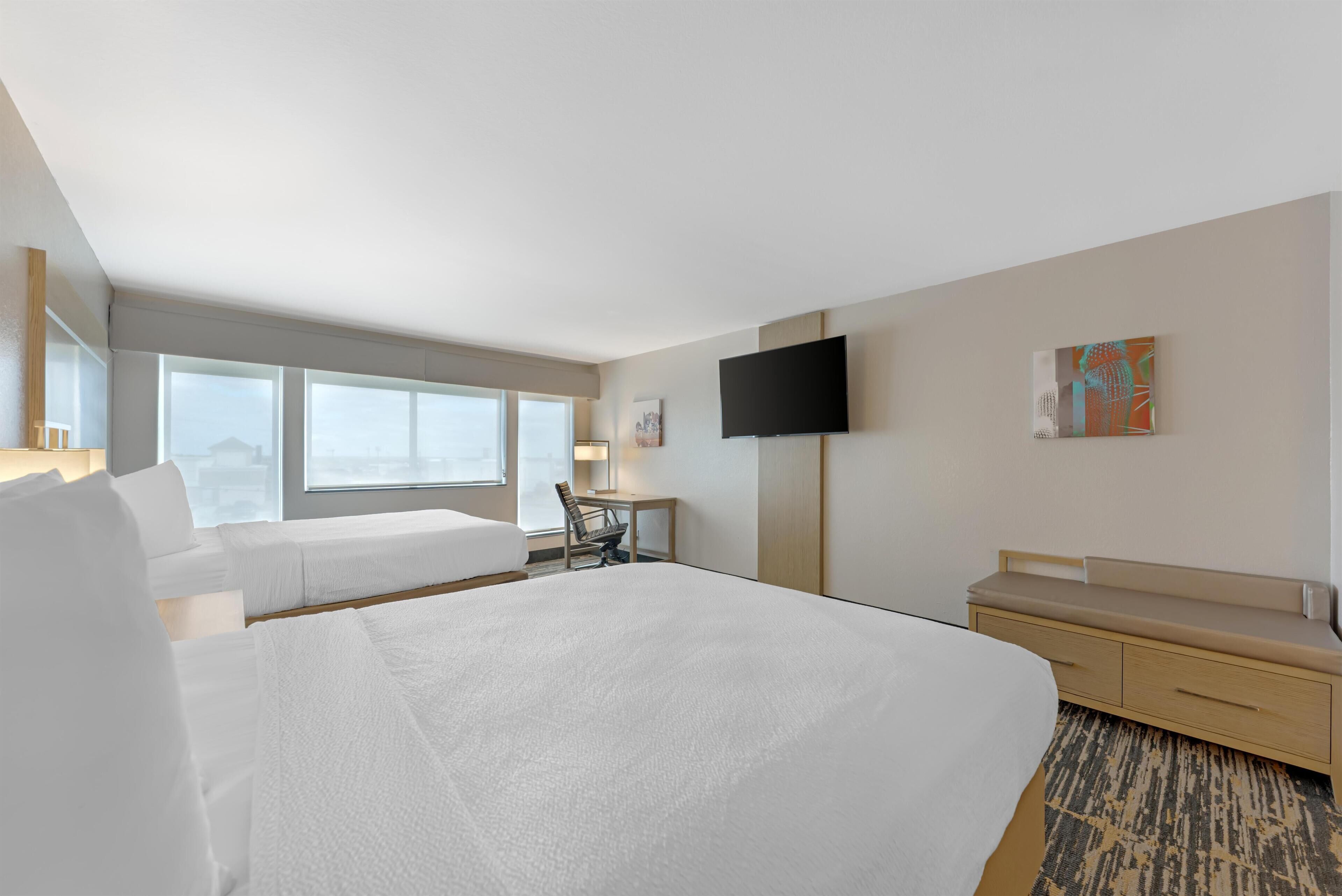 A hotel room with a large bed, a desk, a chair, a TV, and a window with a view.