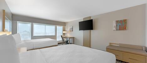 A hotel room with a large bed, a desk, a chair, a TV, and a window with a view.