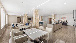 Un comedor moderno con mesas y sillas blancas, pilares de piedra y una encimera con máquinas de café.