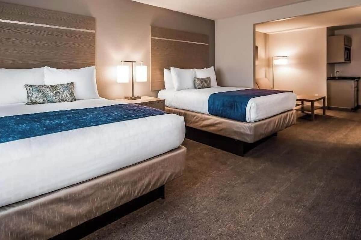 Habitación de hotel con dos camas, una mesita, una mesita de noche y una kitchenette.