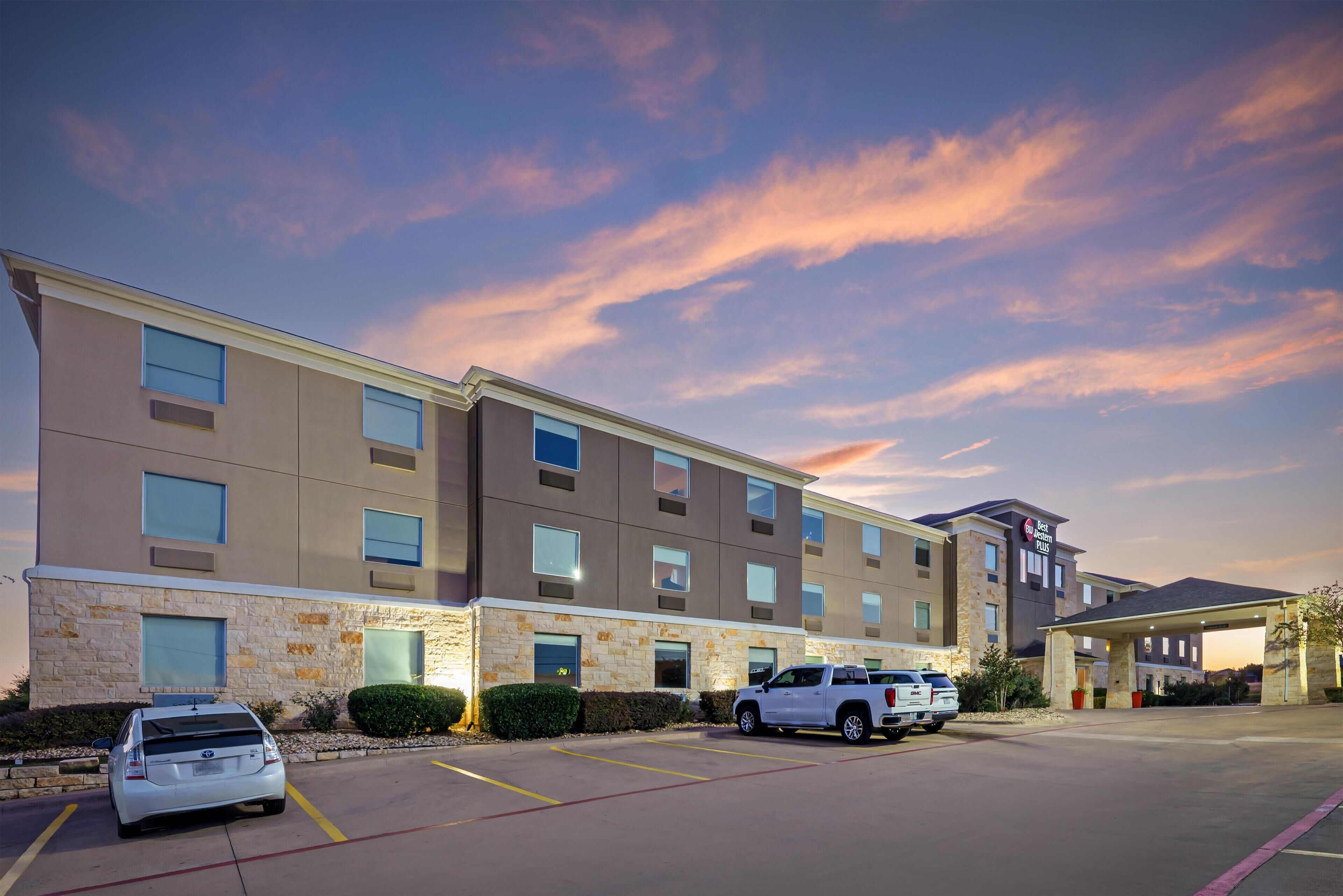 A multi-story hotel with a stone facade, multiple windows, and a parking lot with several vehicles.