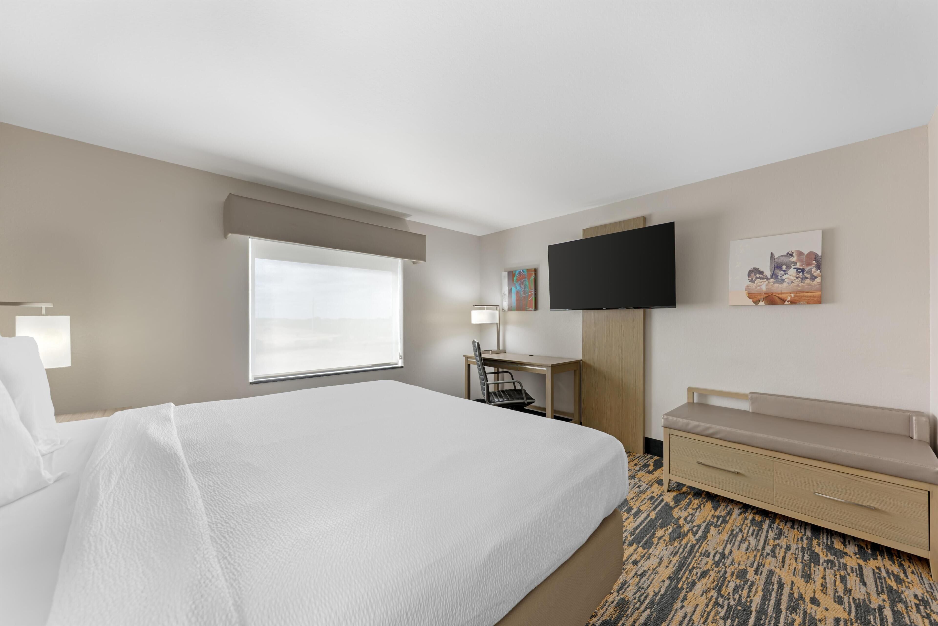 A hotel room with a large bed, a desk, a chair, a TV, and a sofa.