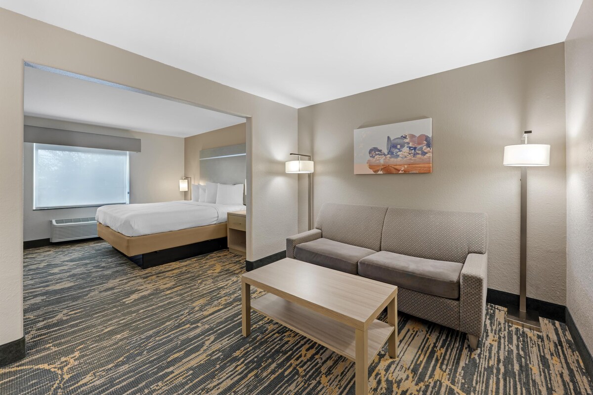 A hotel room with a bed, a sofa, a coffee table, and a painting on the wall.