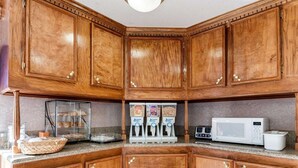 A kitchen with wooden cabinets, a glass display case, a microwave, and a coffee machine. - Econo Lodge Jasper (Jasper)