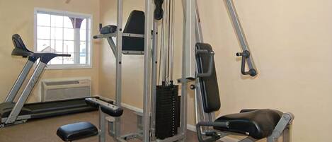 Un gimnasio con una variedad de equipos de ejercicio, incluyendo una prensa de banca, una prensa de piernas y una máquina de poleas.