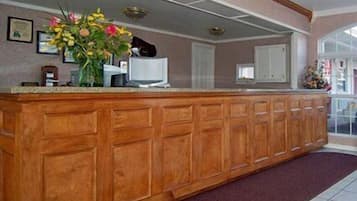 A reception area with a wooden reception desk, a vase of flowers, framed certificates on the wall, and a large window.