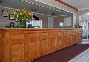 A reception area with a wooden reception desk, a vase of flowers, framed certificates on the wall, and a large window.