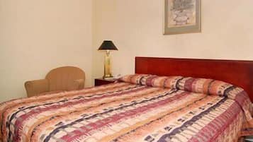 A hotel room with a bed, a chair, a nightstand, a lamp, and a framed picture on the wall.