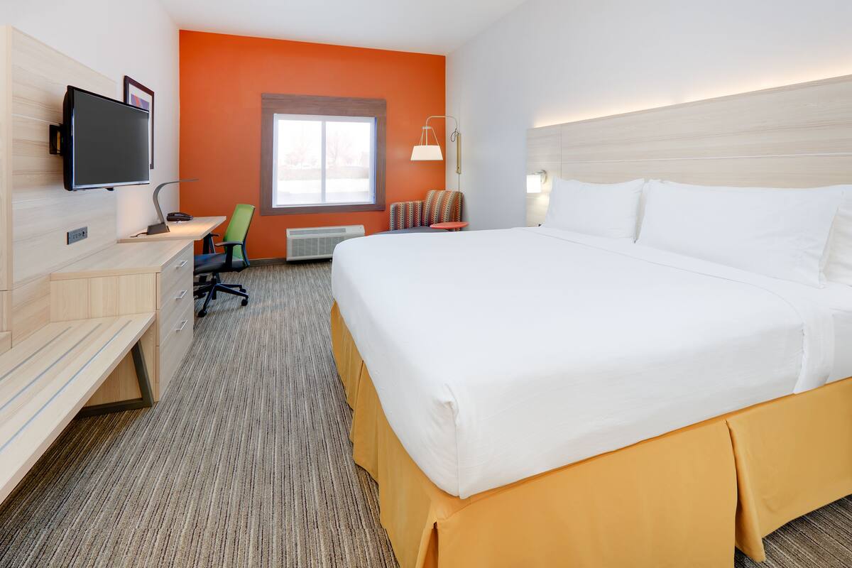 Une chambre d’hôtel avec un grand lit, un bureau avec un ordinateur, une télévision et une fenêtre donnant sur un beau paysage.