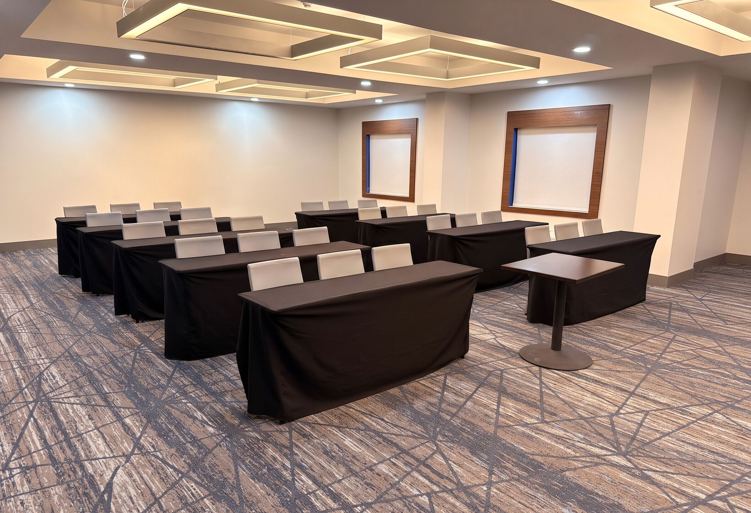Une salle de conférence dotée de plusieurs tables, de chaises et d’un sol recouvert de moquette.