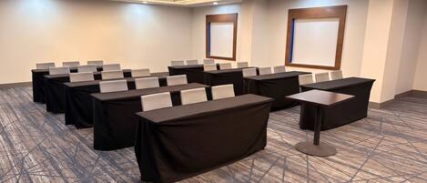 Une salle de conférence dotée de plusieurs tables, de chaises et d’un sol recouvert de moquette.