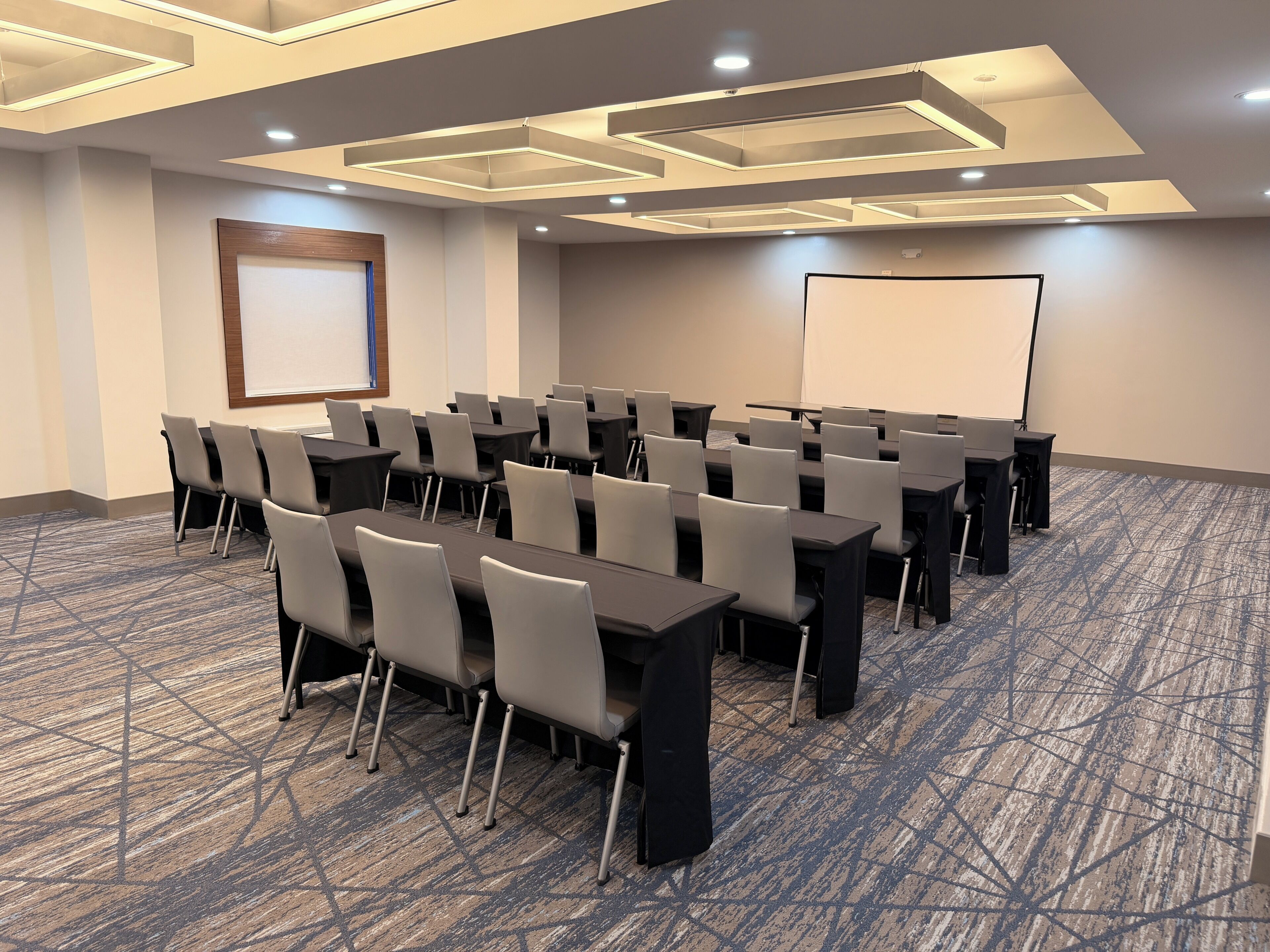 A conference room with tables, chairs, a projector screen, and a carpeted floor.