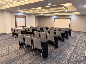 Une salle de conférence équipée de tables, de chaises, d’un écran de projection et d’un sol recouvert de moquette.