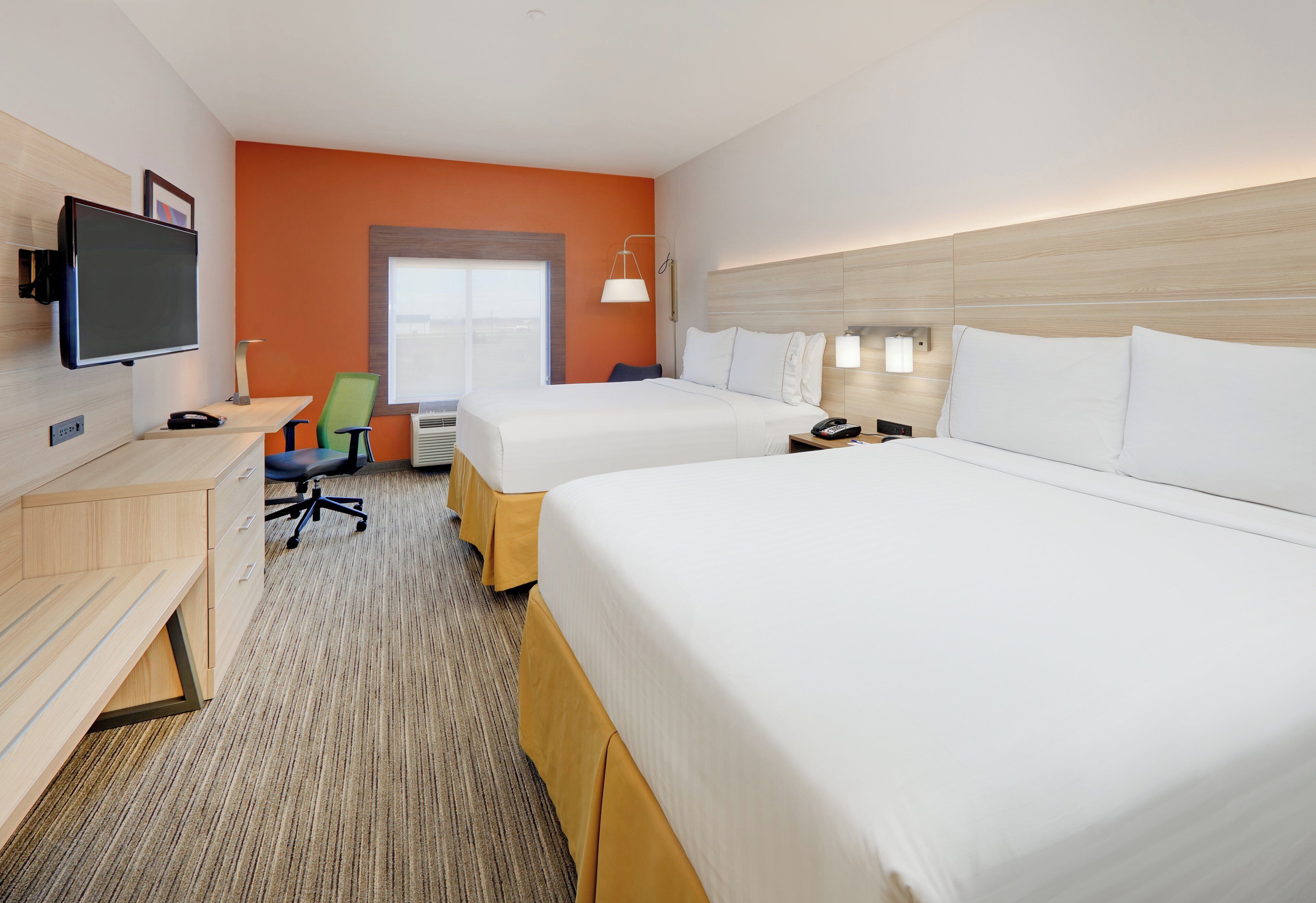 A hotel room with two beds, a desk, a chair, a TV, and a window.