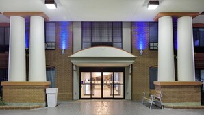 Une entrée d’immeuble avec une façade en briques, de grandes colonnes et une porte d’entrée en verre.