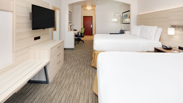 Een hotelkamer met een flatscreen televisie aan de muur, een bureau met stoel, een bed met wit beddengoed en een nachtkastje met een lamp.