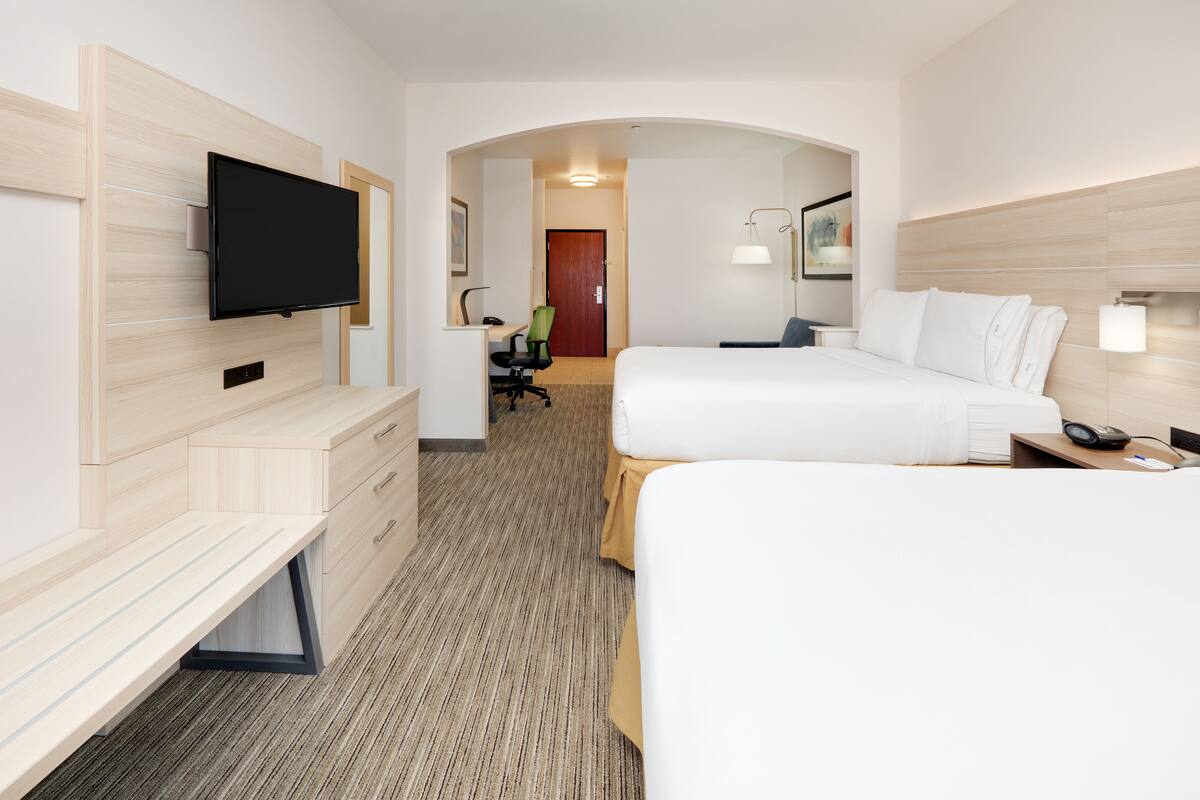 Une chambre d’hôtel équipée d’un téléviseur à écran plat fixé au mur, d’un bureau avec une chaise, d’un lit avec une literie blanche et d’une table de chevet avec une lampe.