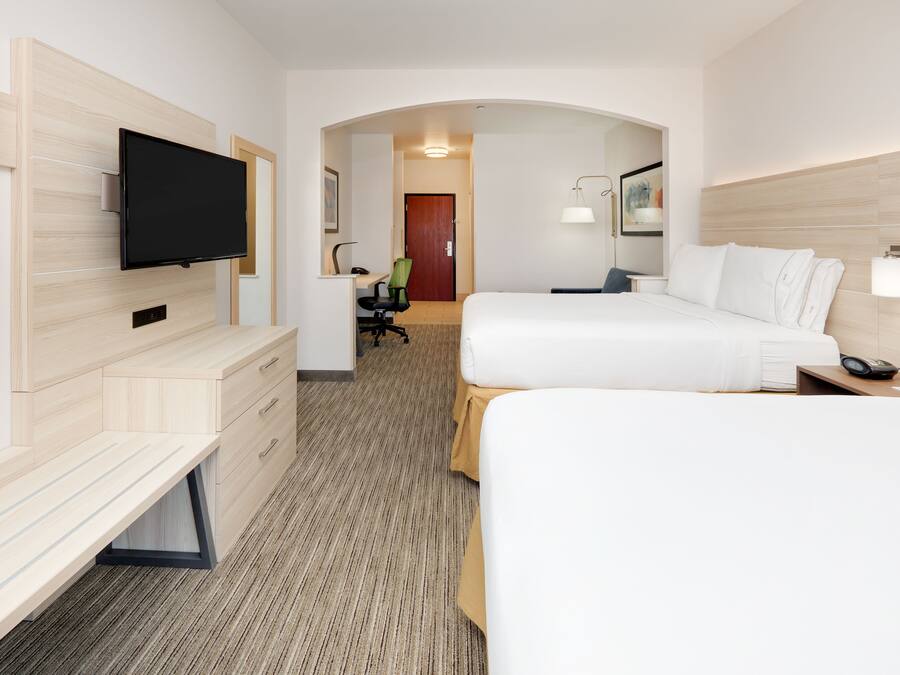 Een hotelkamer met een flatscreen televisie aan de muur, een bureau met stoel, een bed met wit beddengoed en een nachtkastje met een lamp.
