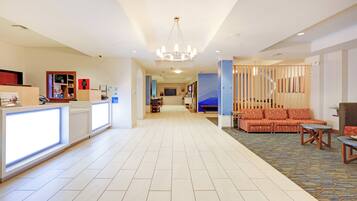 A hotel lobby with a reception desk, seating area, and a chandelier.