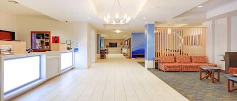 A hotel lobby with a reception desk, seating area, and a staircase leading to upper floors.