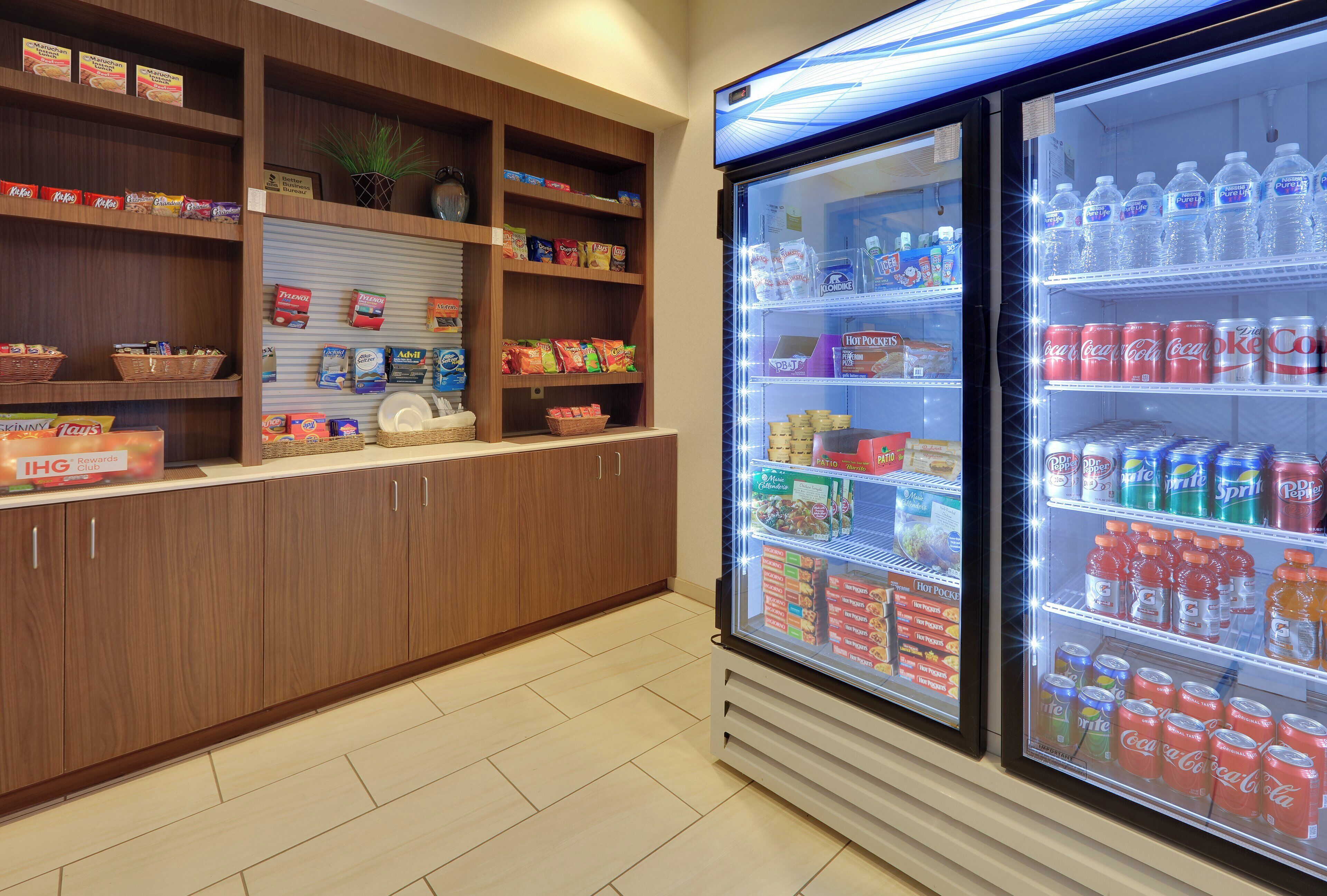 A kitchenette area with a refrigerator stocked with beverages and snacks, a coffee machine, and various food items on shelves.