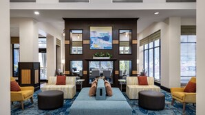 A lobby with a central seating area, large windows, and a modern design. - Hilton Garden Inn West Palm Beach Airport (West Palm Beach)
