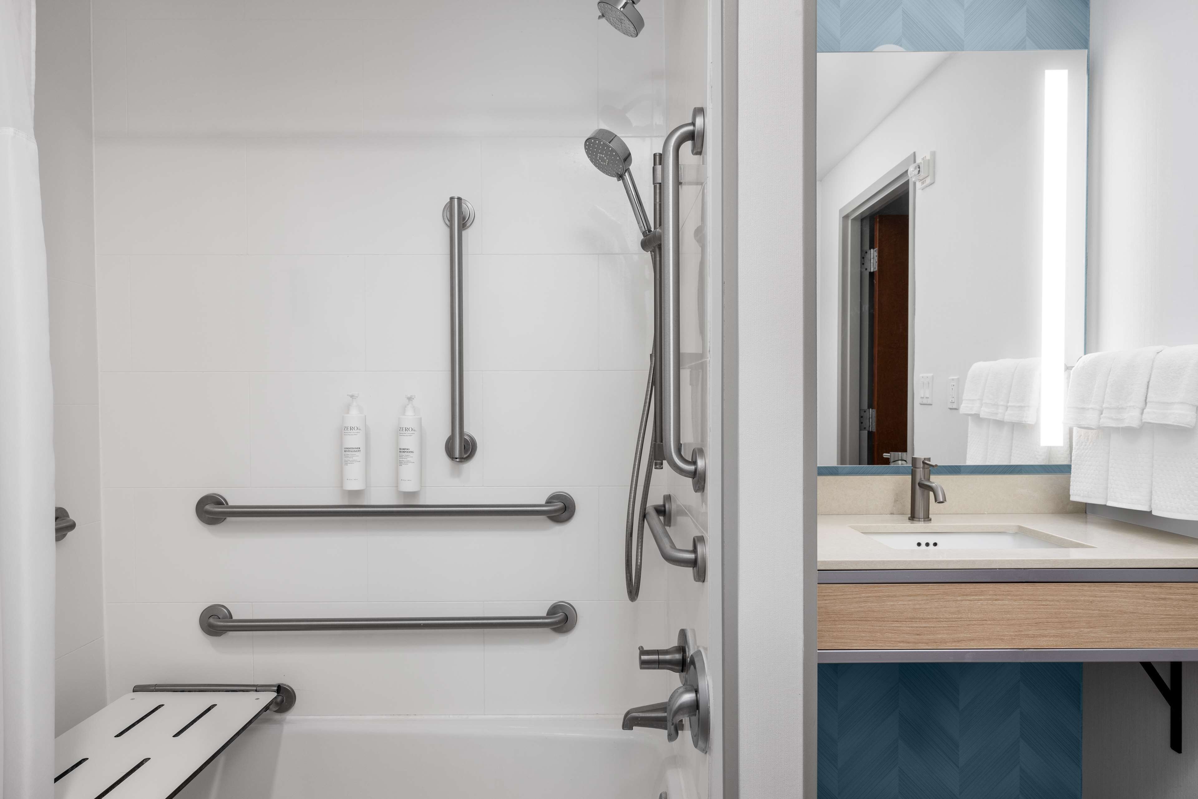 A modern bathroom with a walk-in shower, grab bars, a vanity with a sink, and a mirror.