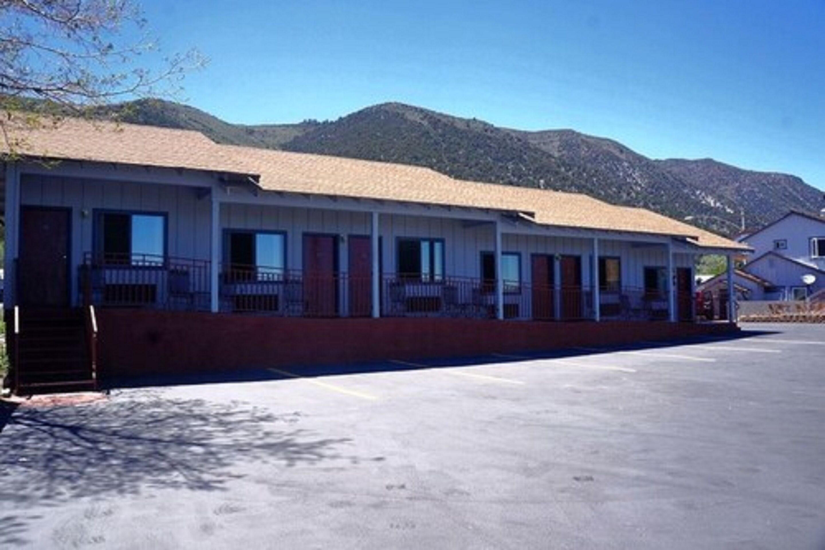 Un motel avec une série de chambres, un parking et des montagnes en arrière-plan.
