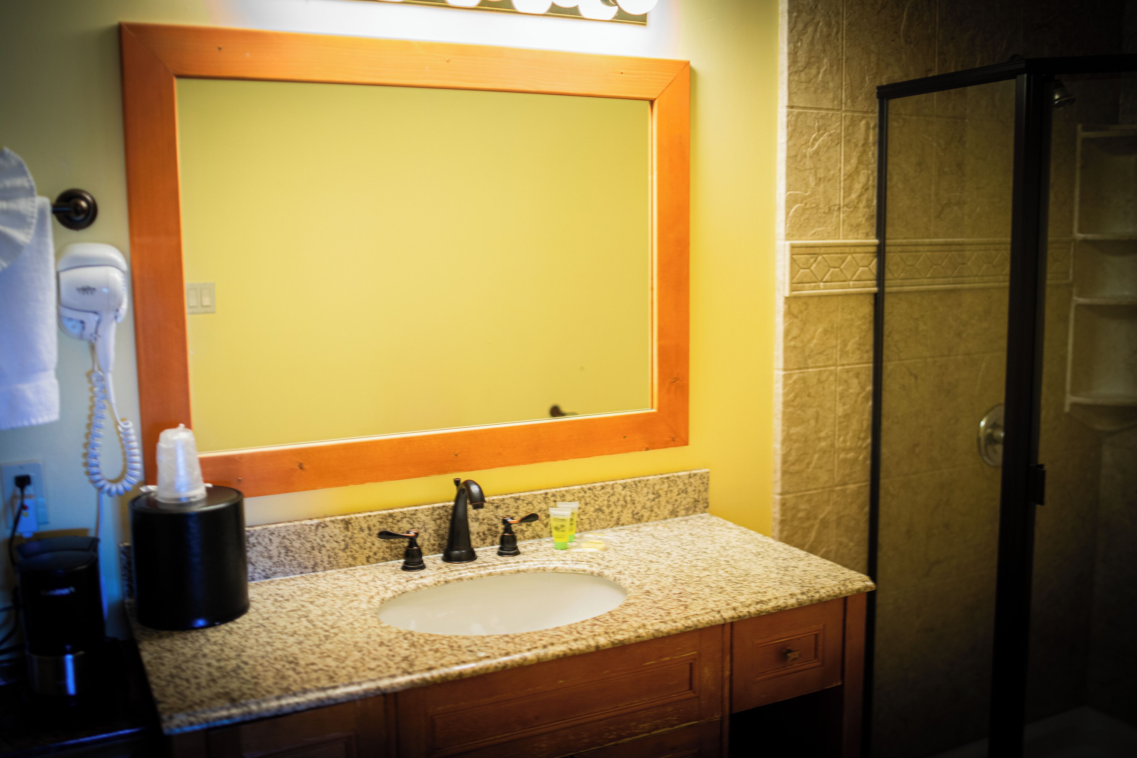 Une salle de bain avec un comptoir en granit, un lavabo, un miroir et une porte de douche.