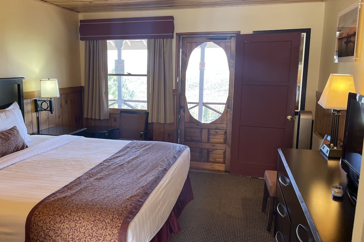 Habitación de hotel con una cama grande, un escritorio con lámpara, una silla, un armario y una puerta con vistas.