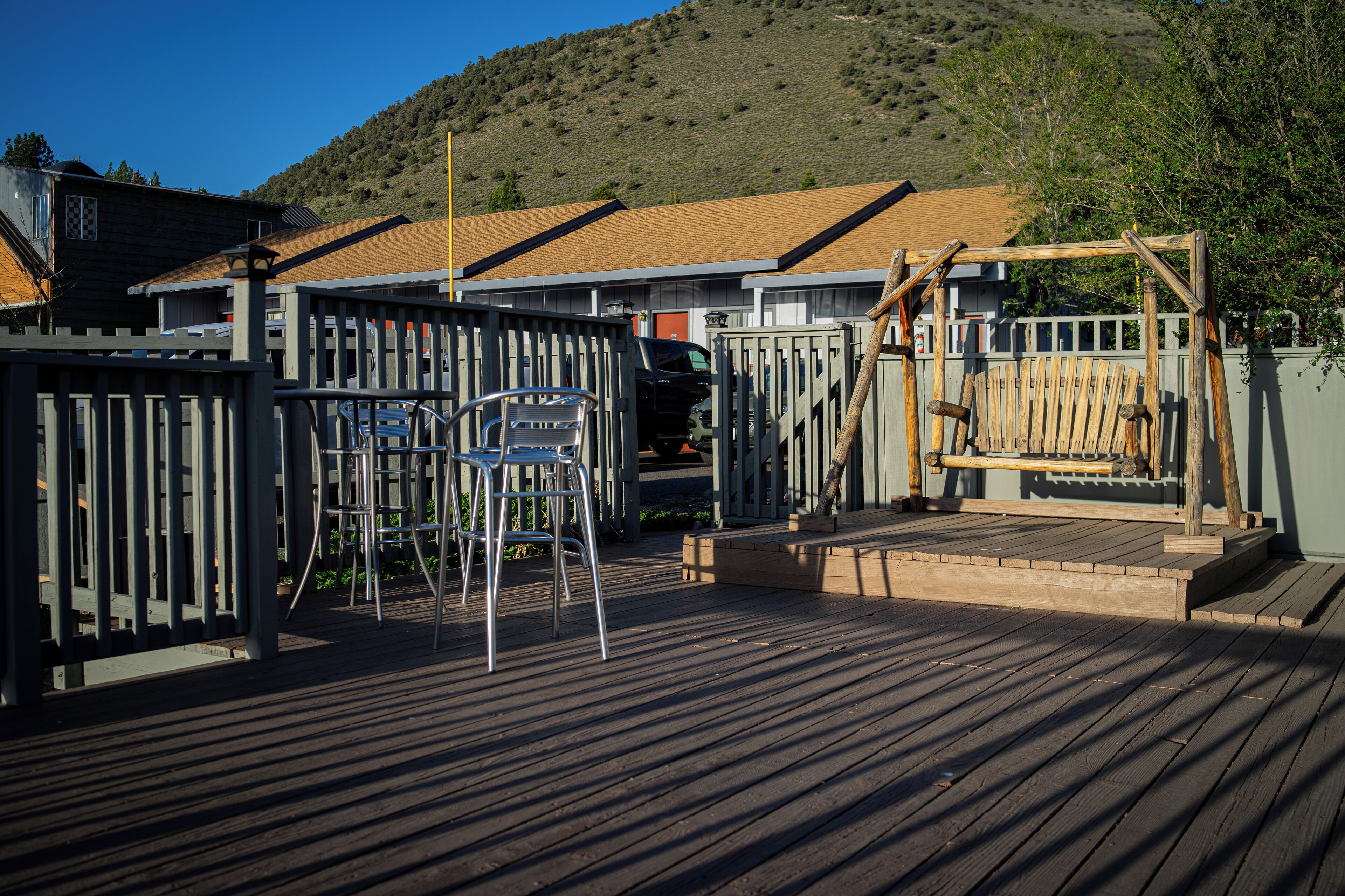 A wooden deck with metal chairs and a wooden swing set.