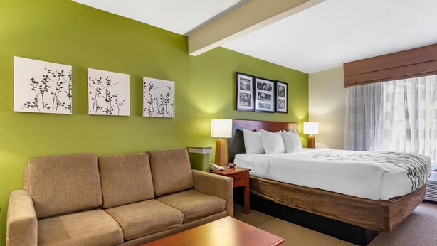 Une chambre d’hôtel avec un mur vert, un canapé, un lit avec une literie blanche et des œuvres d’art accrochées au mur.