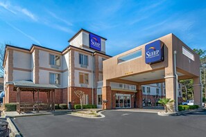 Un bâtiment de la chaîne Sleep Inn & Suites, doté d’une entrée abritée, d’une façade en briques et surplombé d’un ciel bleu clair.