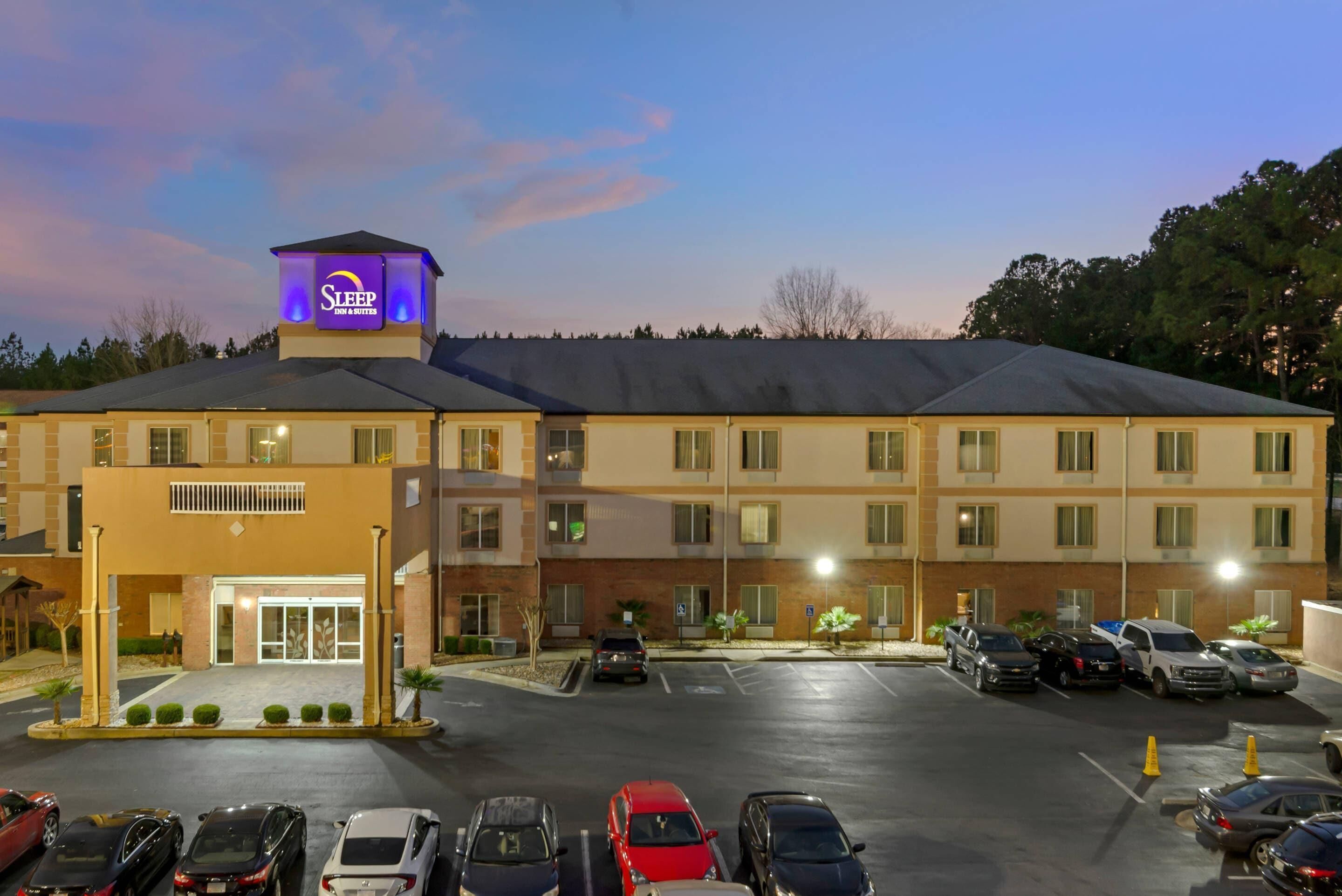 A hotel with a prominent 'Sleep Inn & Suites' sign, a parking lot with several cars, and a well-lit entrance.