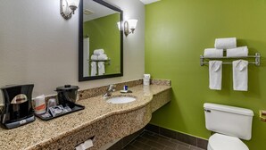 Une salle de bain avec un comptoir en granit, un lavabo, un miroir, des toilettes et un porte-serviettes avec des serviettes.