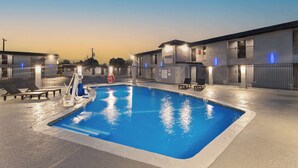 A swimming pool with a lifeguard chair and a ladder, surrounded by a fence and lounge chairs. - GuestHouse Extended Stay Laredo (Laredo)