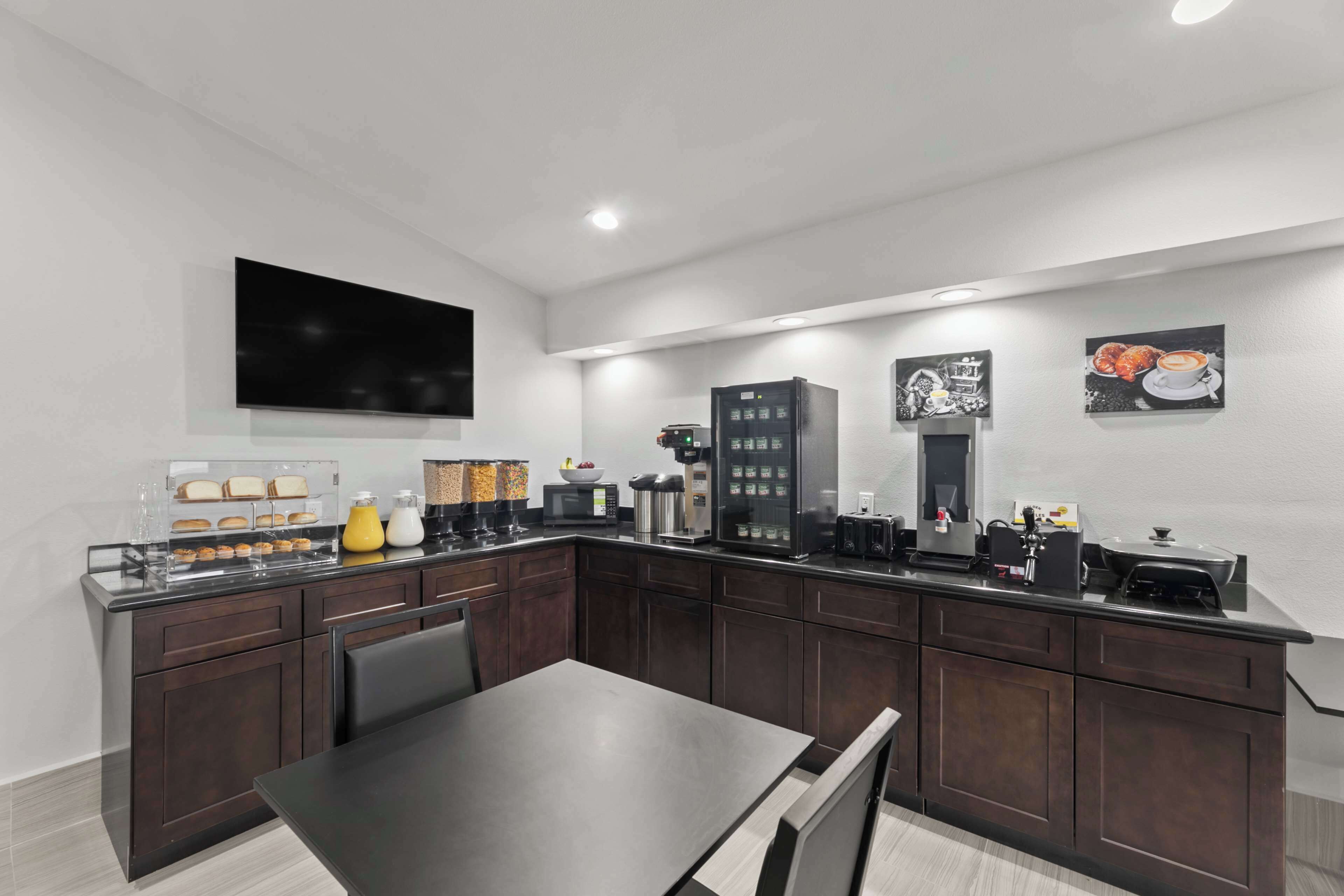 A modern kitchen with dark wood cabinets, a black countertop, and various appliances including a coffee machine and a microwave.