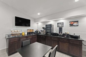 A modern kitchen with dark wood cabinets, a black countertop, and various appliances including a coffee machine and a microwave.