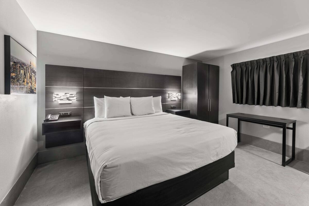A modern hotel room with a large bed, a bedside table with a phone, a nightstand, and a wall-mounted TV.
