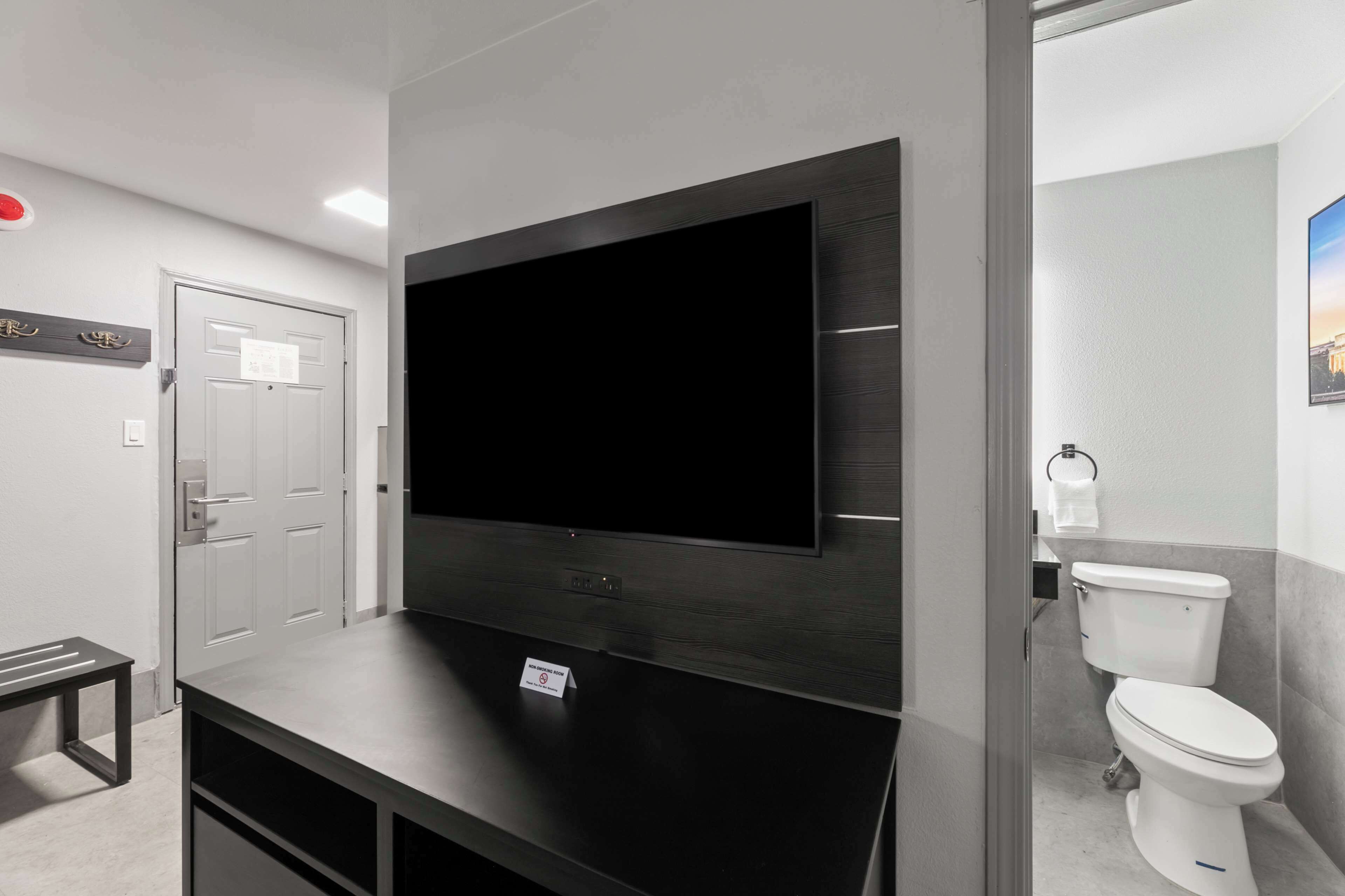 Une salle de bain moderne équipée d’un grand téléviseur à écran plat fixé au mur, de toilettes et d’un banc.