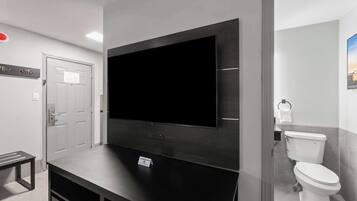 Une salle de bain moderne équipée d’un grand téléviseur à écran plat fixé au mur, de toilettes et d’un banc.