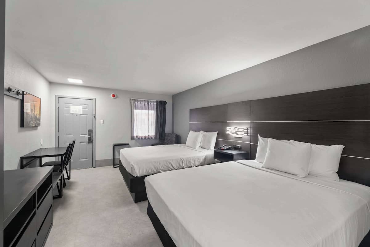 A hotel room with two beds, a desk, and a chair.