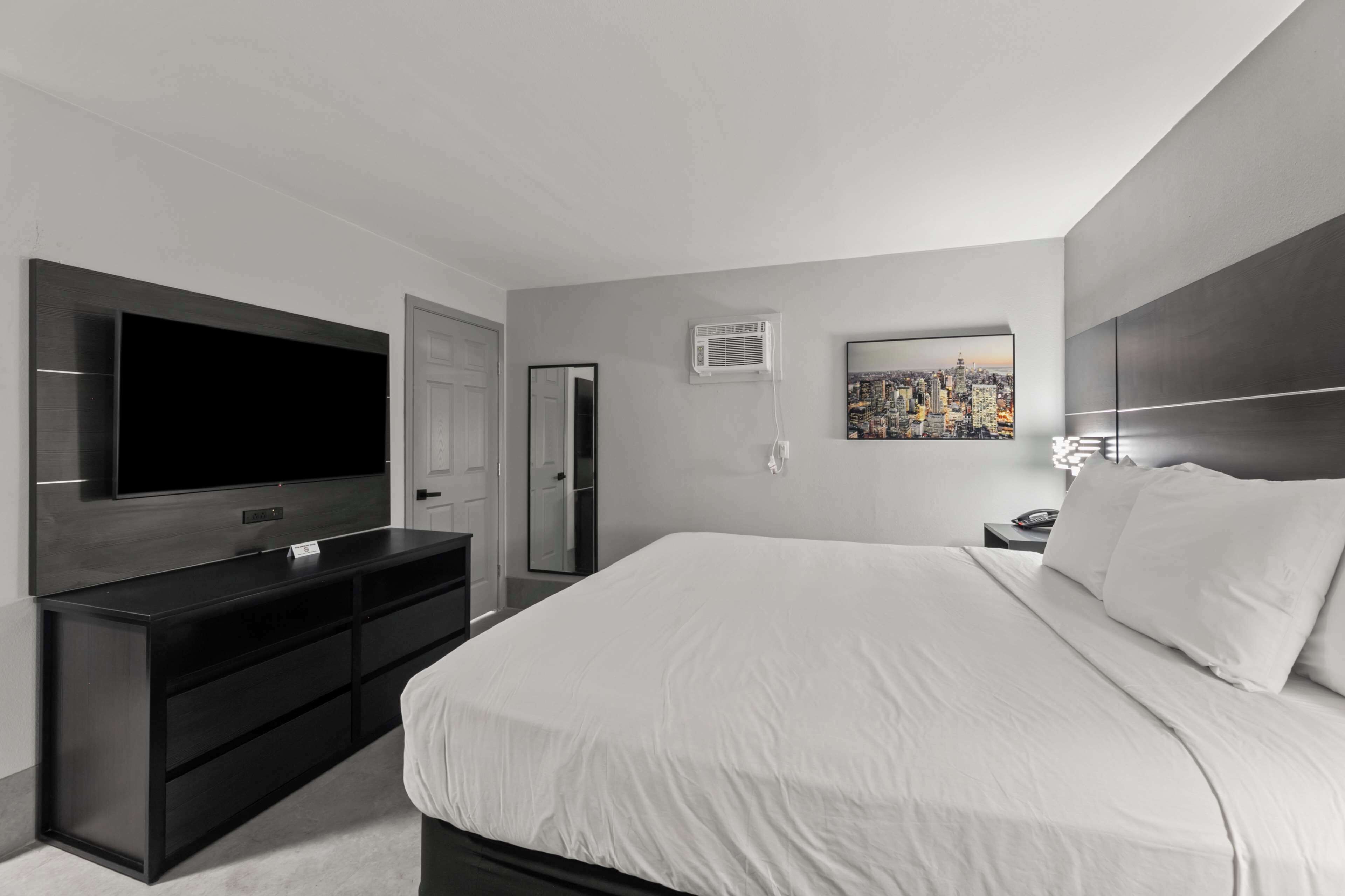 A modern hotel room with a large bed, a flat-screen TV, a built-in wardrobe, and a cityscape painting on the wall.