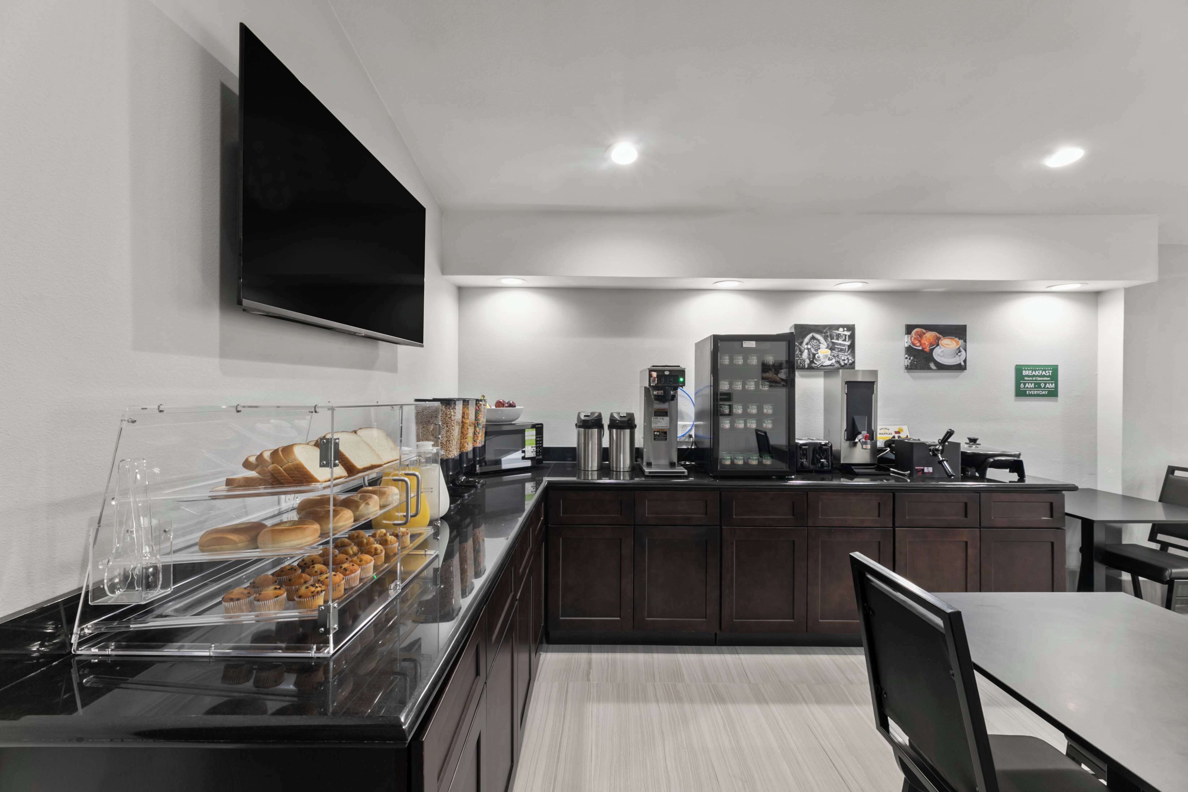 A modern kitchen with a breakfast bar, a coffee machine, and a flat-screen TV mounted on the wall.