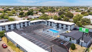 A large parking lot with a swimming pool, surrounded by a building with multiple floors and a sign indicating it's a guest house.