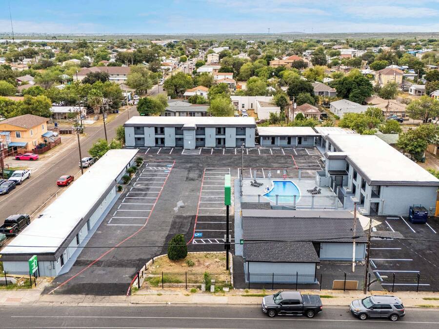 Un edificio grande con piscina, varios espacios de estacionamiento y vista a la calle.