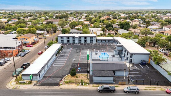 A large building with a swimming pool, multiple parking spaces, and a street view.