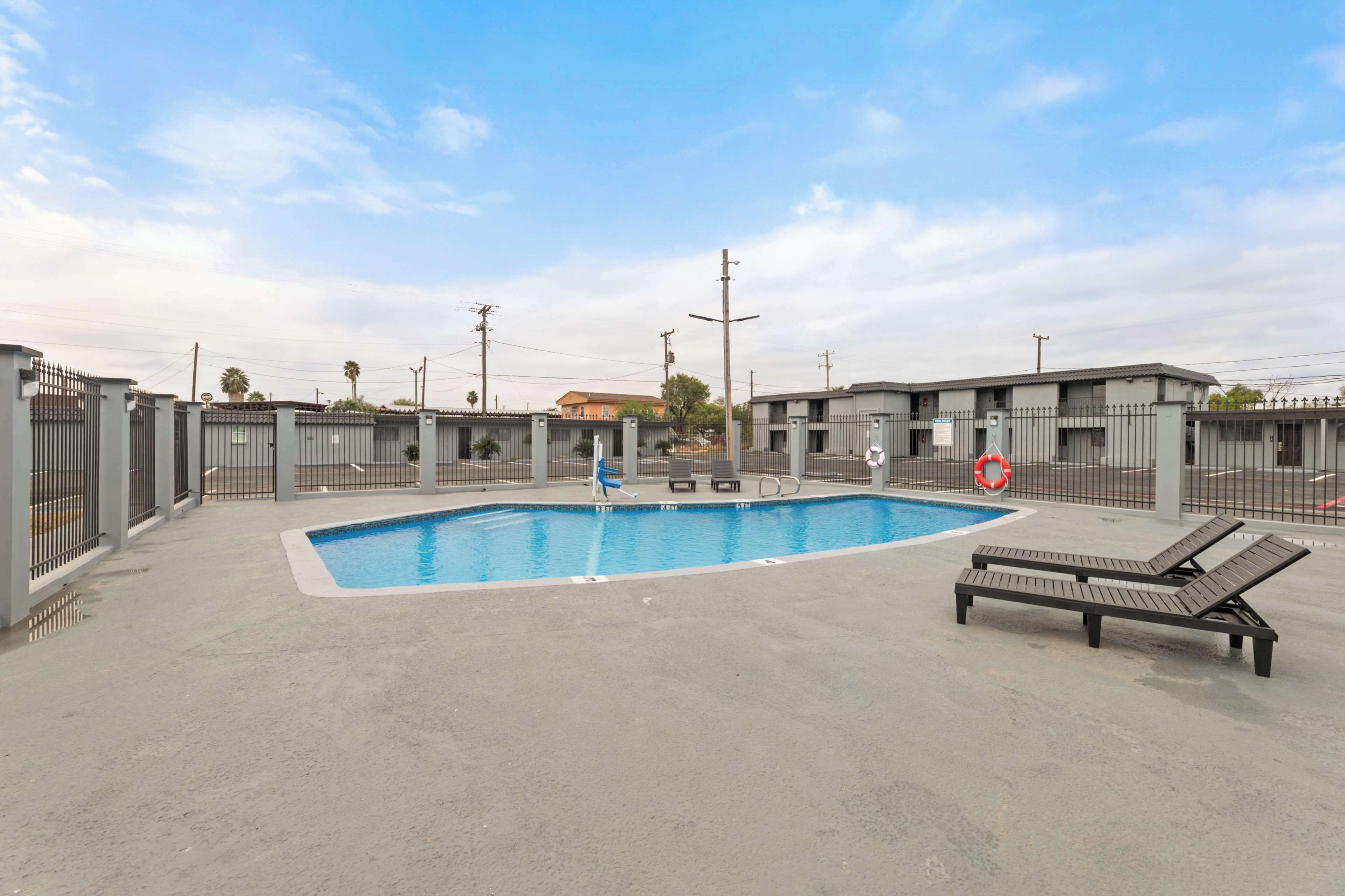 Una piscina con un flotador salvavidas, sillas de descanso y una zona vallada con un edificio al fondo.